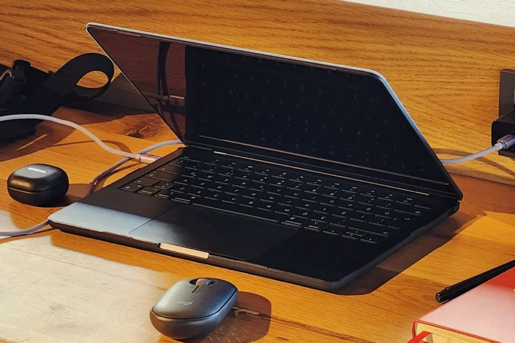 An open laptop with a wireless mouse and charging cables on a wooden desk.